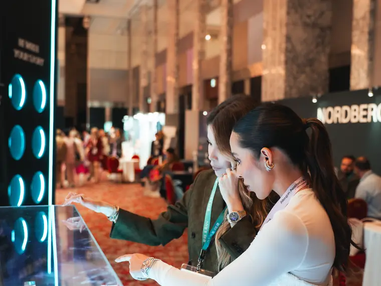 Duas médicas em pé diante de uma vitrine iluminada de produtos, no AMWC Japão